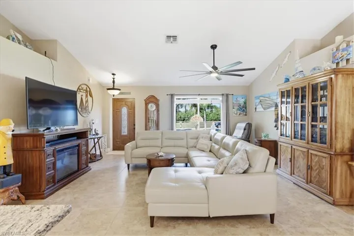 Living room with lofted ceiling, a ceiling fan, a glass covered fireplace, and light tile patterned floors