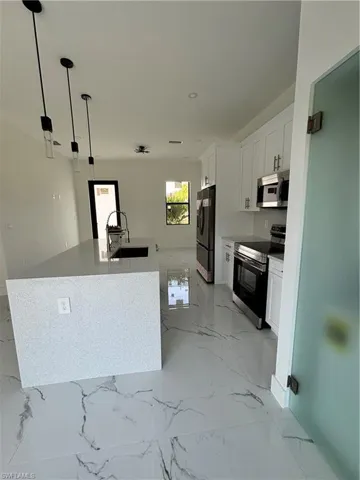 Kitchen featuring white cabinets, range, marble finish floor, refrigerator, and a sink