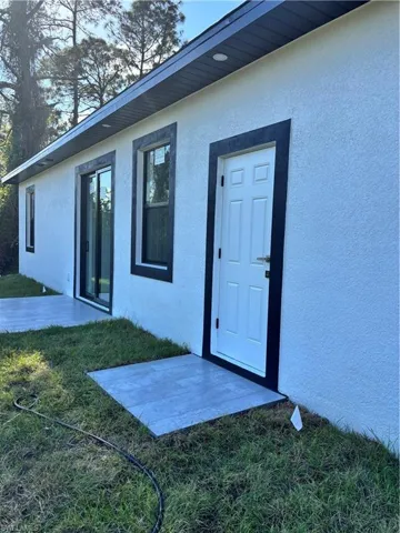 Property entrance with a patio area, stucco siding, and a lawn