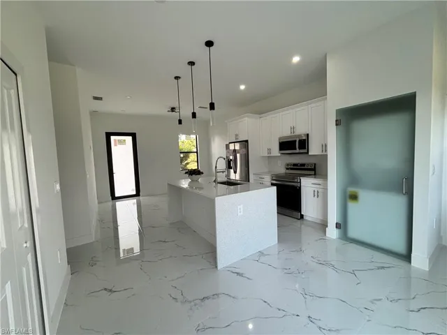 Kitchen with marble finish floor, a center island with sink, a sink, stainless steel appliances, and white cabinets