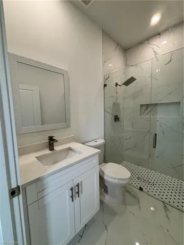 Full bath featuring a marble finish shower, toilet, marble finish floor, and vanity