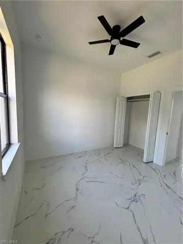 Unfurnished bedroom with a ceiling fan, marble finish floor, visible vents, and a closet