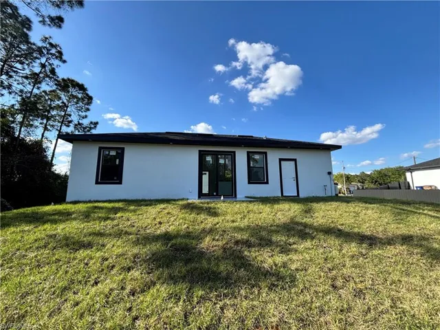 Back of property with a lawn, fence, and stucco siding
