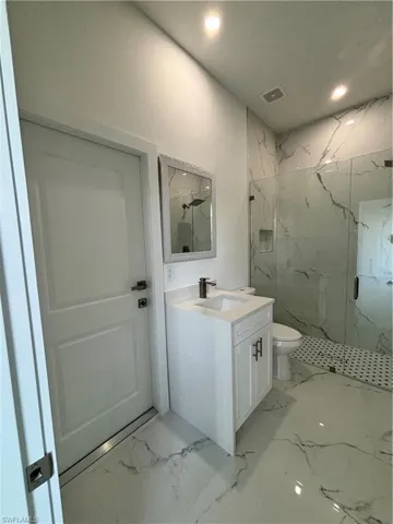 Bathroom featuring visible vents, toilet, marble finish floor, a marble finish shower, and vanity