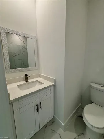 Bathroom with vanity, toilet, baseboards, and marble finish floor