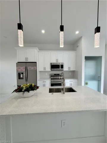 Kitchen featuring backsplash, stainless steel range with electric stovetop, refrigerator, white cabinetry, and a sink