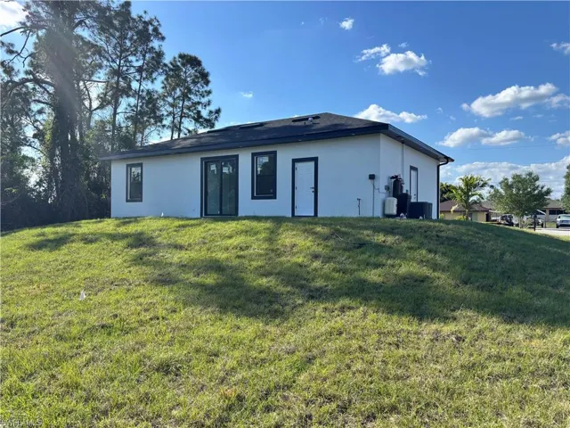 Back of house with stucco siding, central air condition unit, and a lawn