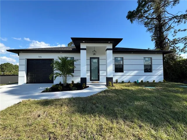 View of front facade with stucco siding, an attached garage, concrete driveway, and a front lawn