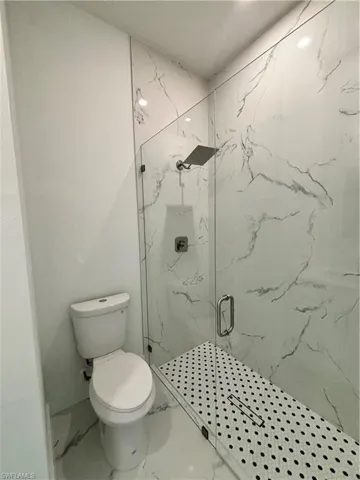 Bathroom with toilet, marble finish floor, and a marble finish shower