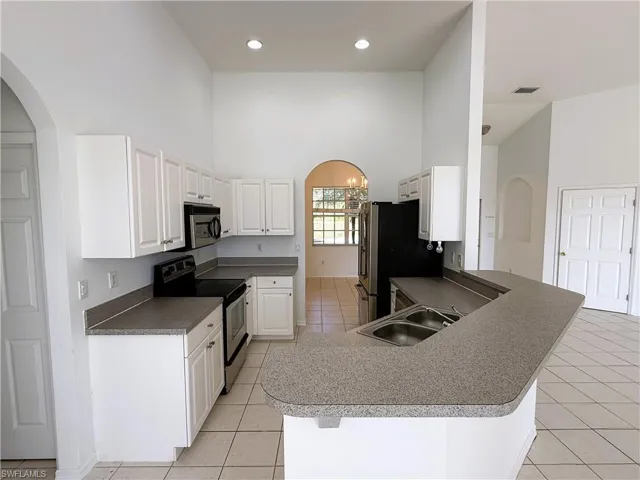 Kitchen featuring arched walkways, a high ceiling, appliances with stainless steel finishes, white cabinetry, and a peninsula