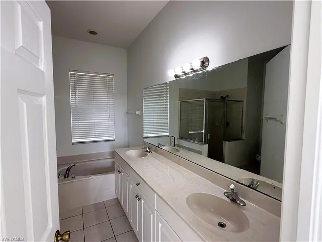 Full bath featuring a shower stall, double vanity, a garden tub, and light tile patterned floors
