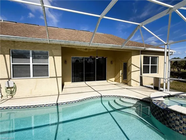 Back of property with a sunroom, a pool with connected hot tub, roof with shingles, stucco siding, and a patio