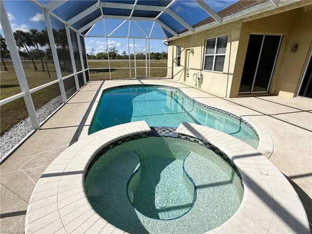 View of swimming pool with a patio area, a pool with connected hot tub, a sunroom, and glass enclosure