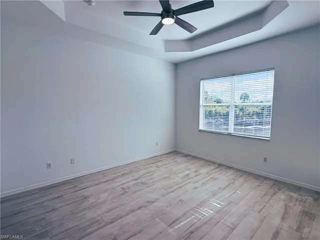 Empty room with a tray ceiling, light wood-style floors, and ceiling fan
