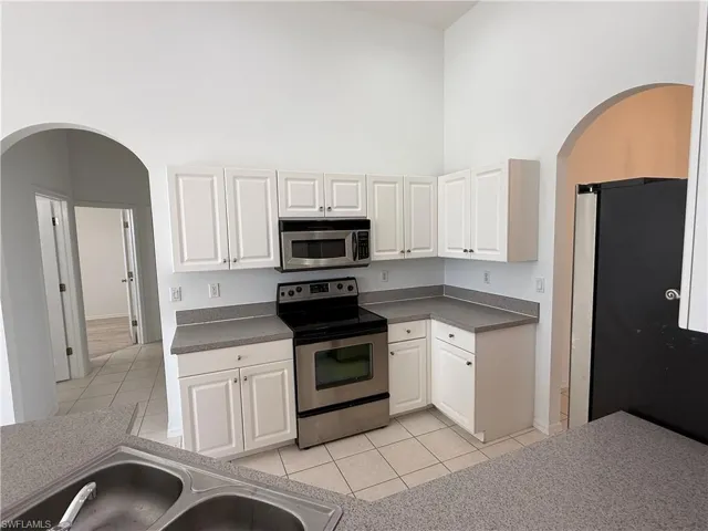 Kitchen with arched walkways, stainless steel appliances, white cabinetry, light tile patterned flooring, and a high ceiling
