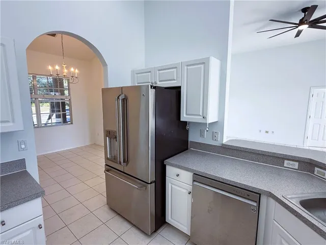 Kitchen featuring a chandelier, appliances with stainless steel finishes, light tile patterned floors, white cabinetry, and a towering ceiling