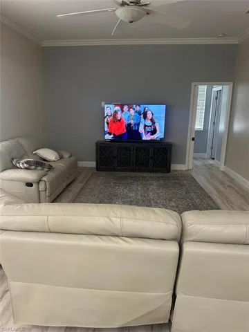 Living room with crown molding, a ceiling fan, and wood finished floors
