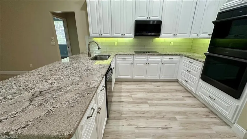 Kitchen with light stone counters, black appliances, white cabinetry, backsplash, and light wood-style flooring