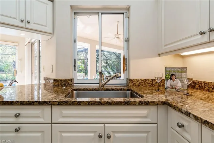 Kitchen featuring ceiling fan, granite countertops, sink, and white cabinets