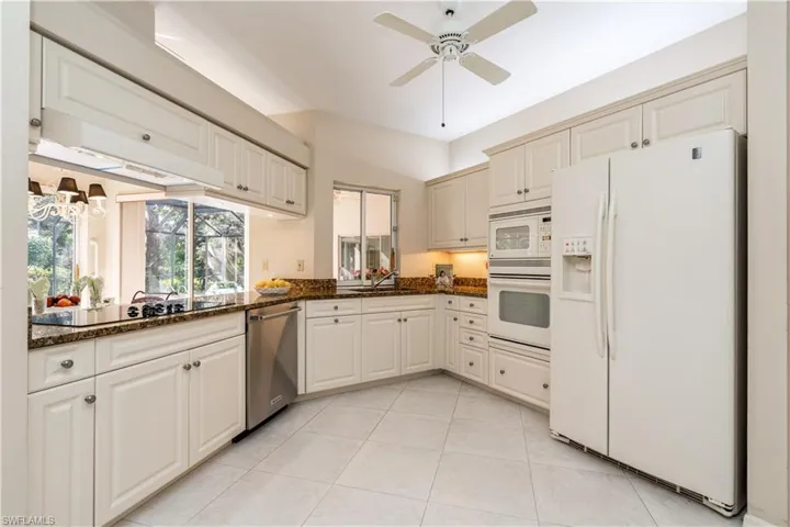 Kitchen featuring light tile patterned flooring, sink, dark stone countertops, ceiling fan, and white appliances