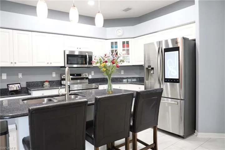 Kitchen with a kitchen bar, appliances with stainless steel finishes, white cabinetry, and hanging light fixtures