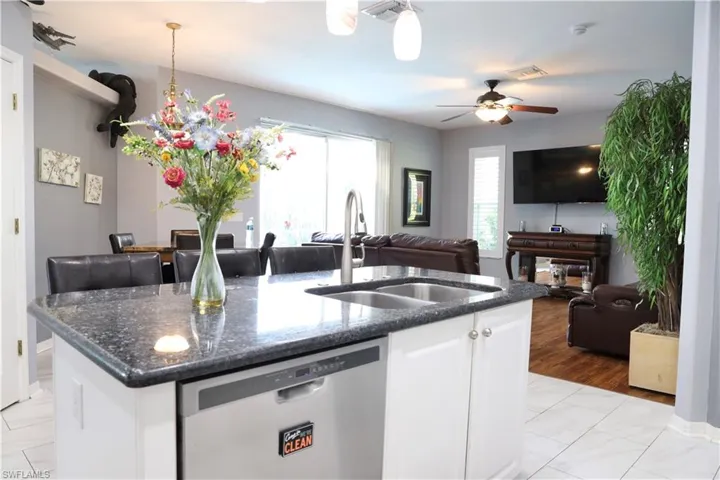Kitchen with dishwasher, white cabinets, sink, granite countertops, and an island with sink