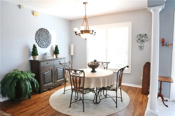 Dining area featuring wood-style vinyl flooring, a notable chandelier, and decorative columns
