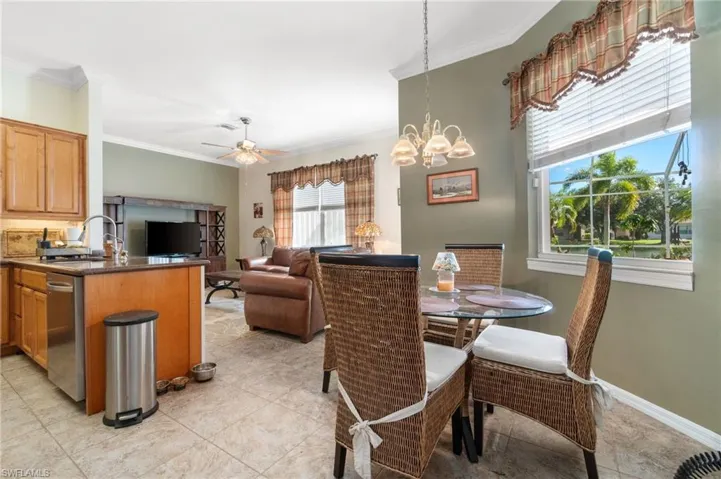 Tiled dining area with sink, ceiling fan with notable chandelier, and crown molding