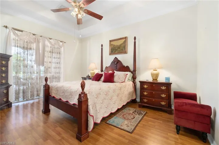 Bedroom with wood-type flooring, a raised ceiling, ornamental molding, and ceiling fan