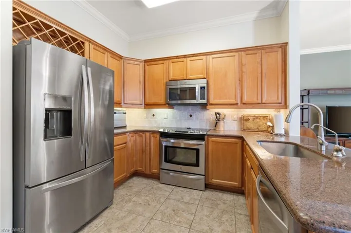 Kitchen with stainless steel appliances, sink, backsplash, dark stone countertops, and ornamental molding