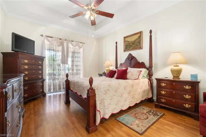 Bedroom with a raised ceiling, ornamental molding, hardwood / wood-style floors, and ceiling fan