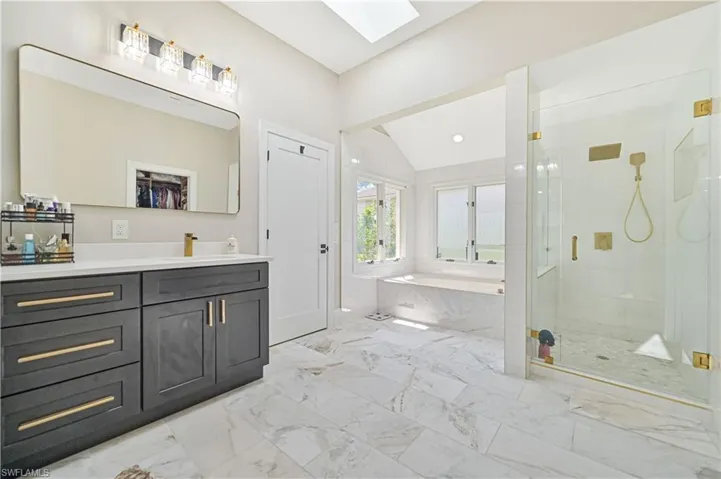 Bathroom with tile patterned floors, independent shower and bath, vanity, and vaulted ceiling with skylight
