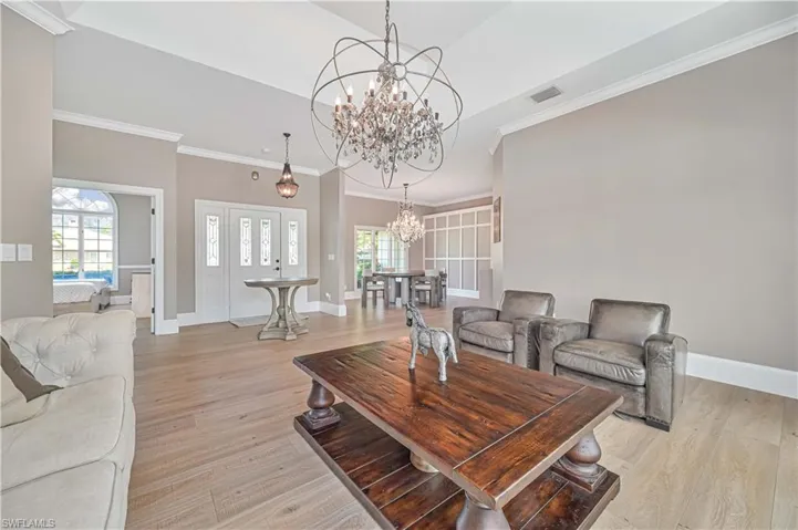 Living room with a wealth of natural light, an inviting chandelier, light hardwood / wood-style floors, and ornamental molding