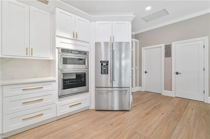 Kitchen featuring stainless steel appliances, light hardwood / wood-style floors, ornamental molding, tasteful backsplash, and white cabinets