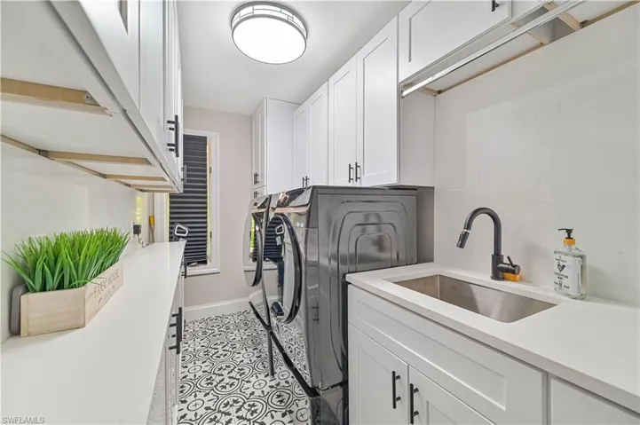 Laundry area with light tile patterned floors, sink, separate washer and dryer, and cabinets