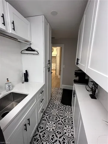 Kitchen with white cabinets, sink, light stone countertops, and light hardwood / wood-style floors