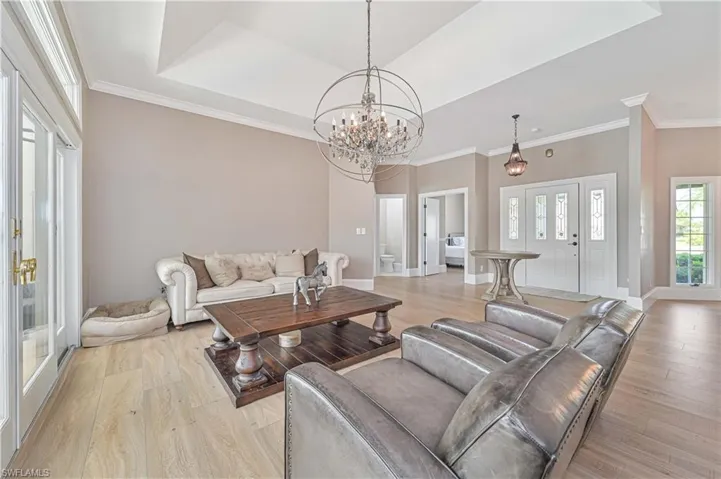 Living room featuring crown molding, a raised ceiling, an inviting chandelier, and light wood-type flooring