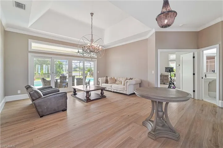 Living room with light wood-type flooring, a tray ceiling, french doors, an inviting chandelier, and crown molding