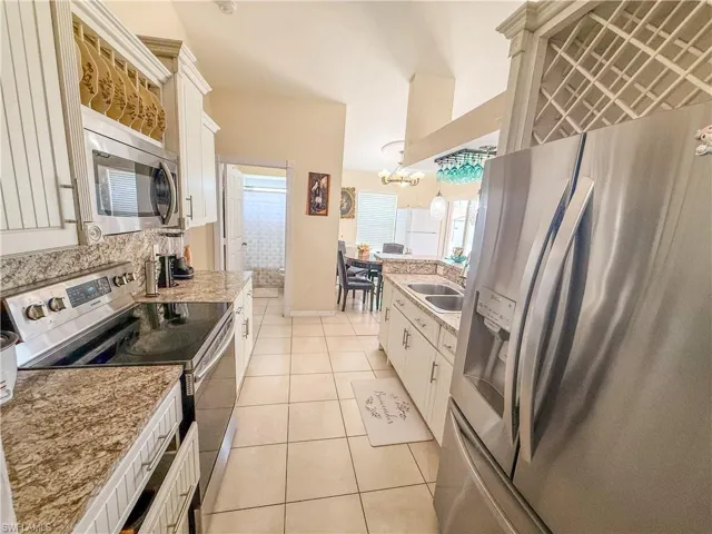 Kitchen with light stone countertops, a sink, white cabinets, stainless steel appliances, and light tile patterned flooring
