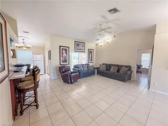 Living room featuring visible vents, light tile patterned floors, vaulted ceiling, and ceiling fan with notable chandelier