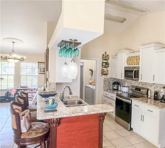 Kitchen featuring an inviting chandelier, a sink, stainless steel appliances, decorative backsplash, and light tile patterned floors