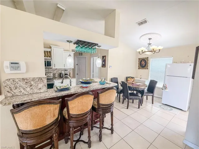 Dining room with vaulted ceiling, a notable chandelier, light tile patterned flooring, and visible vents