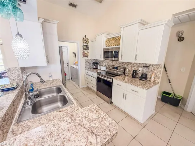 Kitchen featuring decorative backsplash, visible vents, appliances with stainless steel finishes, a sink, and light countertops