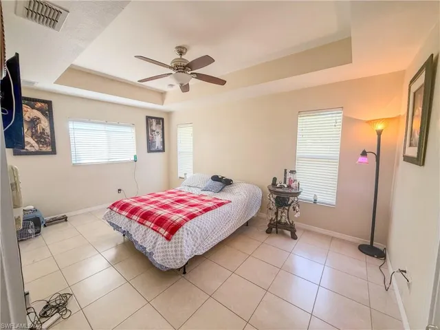 Bedroom featuring visible vents, baseboards, light tile patterned flooring, and a tray ceiling