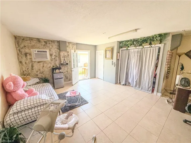 Living room with an AC wall unit, a textured ceiling, light tile patterned floors, and an accent wall