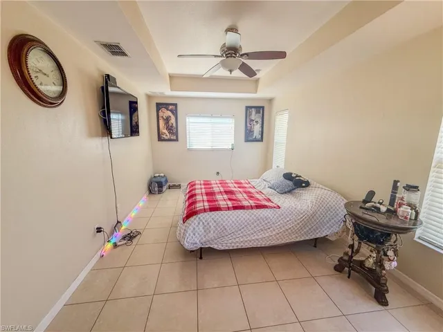 Bedroom with ceiling fan, visible vents, tile patterned flooring, baseboards, and a raised ceiling