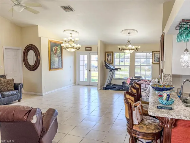 Living area featuring french doors, ceiling fan with notable chandelier, baseboards, light tile patterned floors, and visible vents