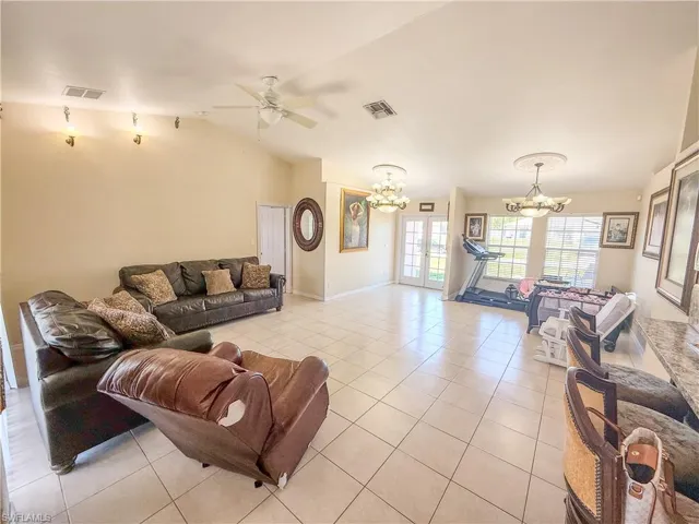 Living area featuring light tile patterned flooring, visible vents, french doors, and ceiling fan with notable chandelier