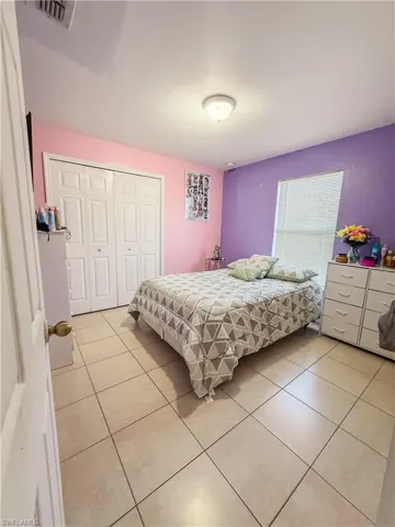 Bedroom with a closet, light tile patterned floors, and visible vents