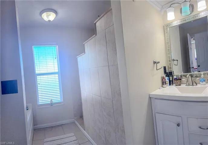 Bathroom featuring vanity, tile patterned floors, a bathtub, baseboards, and a shower